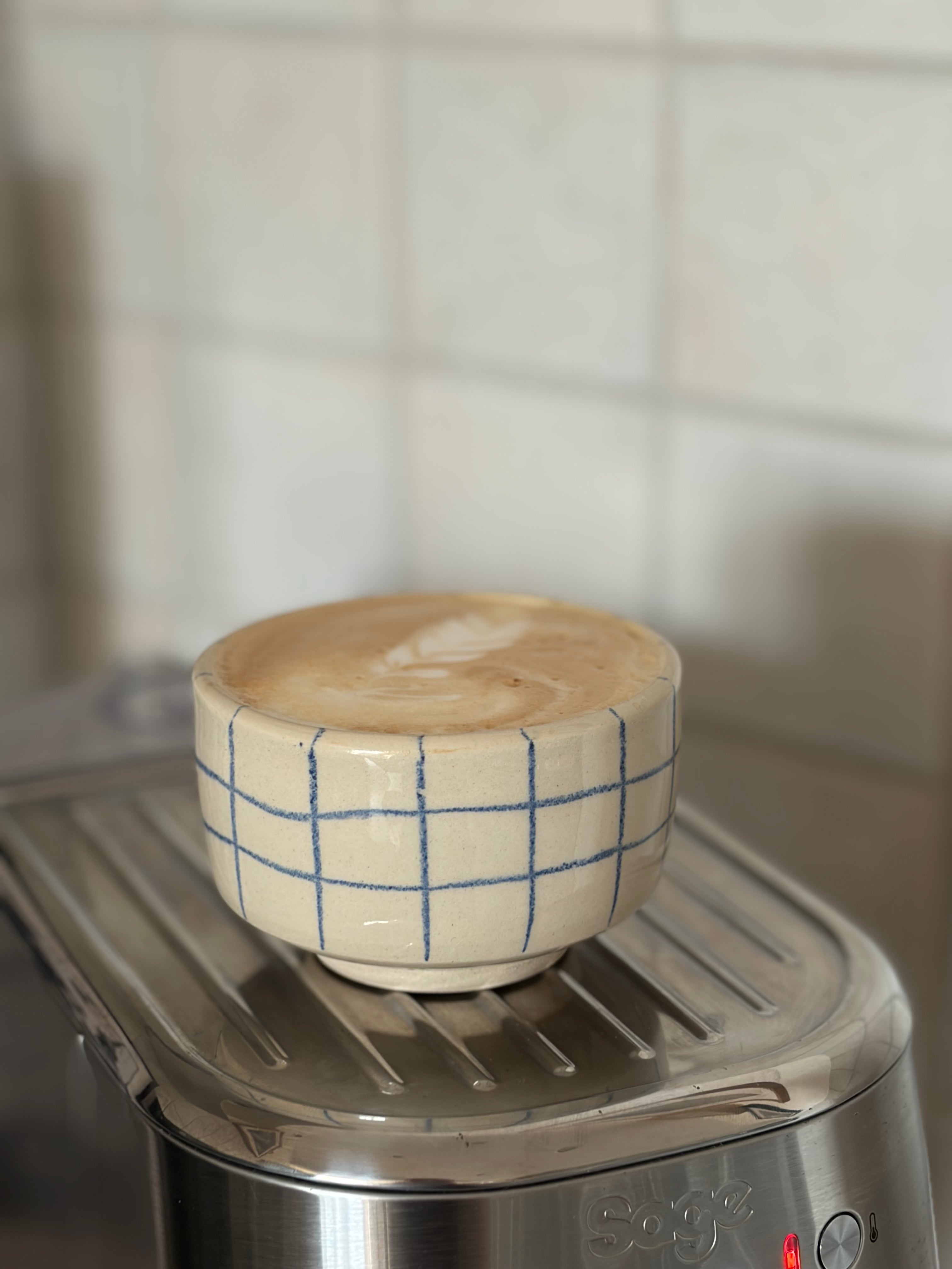 Handgedrehter Keramikbecher blau kariert mit Cappuccino, auf Espressomaschine