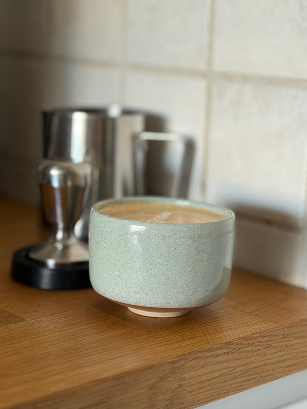 Handgedrehter Keramikbecher in Pastellmint mit Cappuccino, auf Holzarbeitsplatte neben Espressomaschine