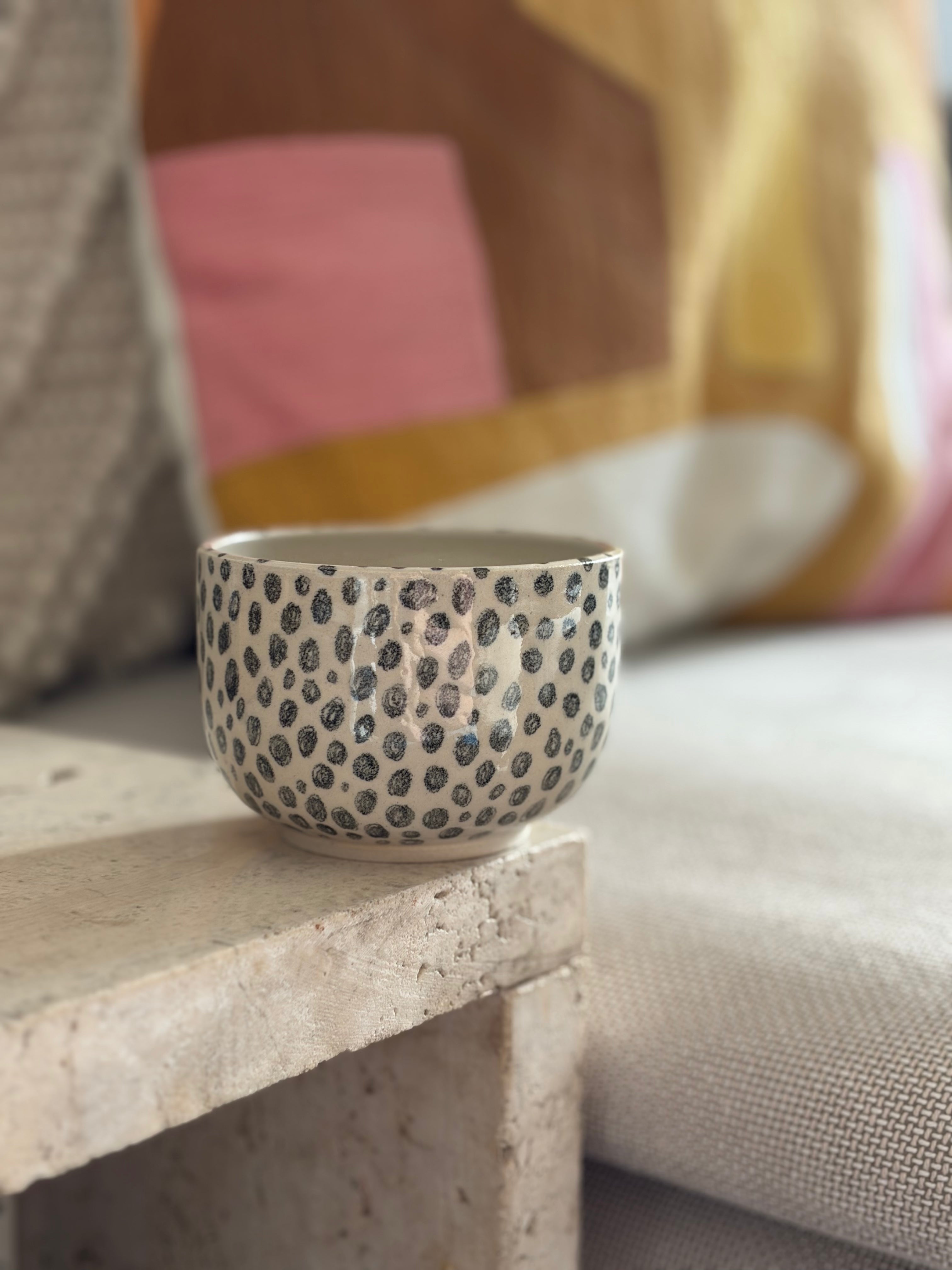 Keramikbecher aus weißem Ton mit schwarzen punkten, in Sofaecke 