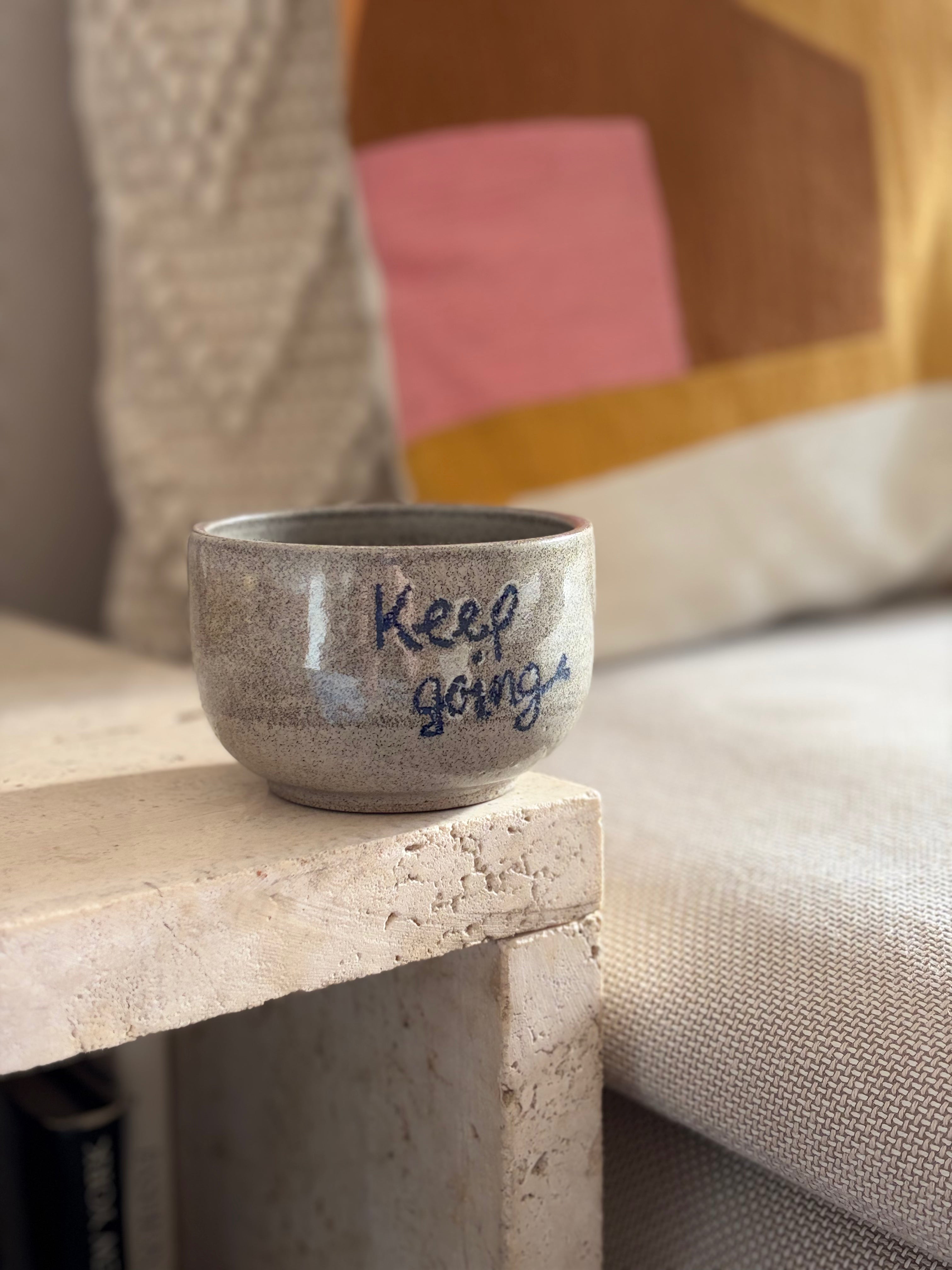 Grauer handgemachter Keramikbecher mit der Aufschrift "Keep going" in Sofaecke 