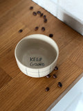 Keramikbecher, handgedreht mit einer Innschrift in schwarz 'keep going'. Von aussen schwarz kariert, auf Küchenzeile 