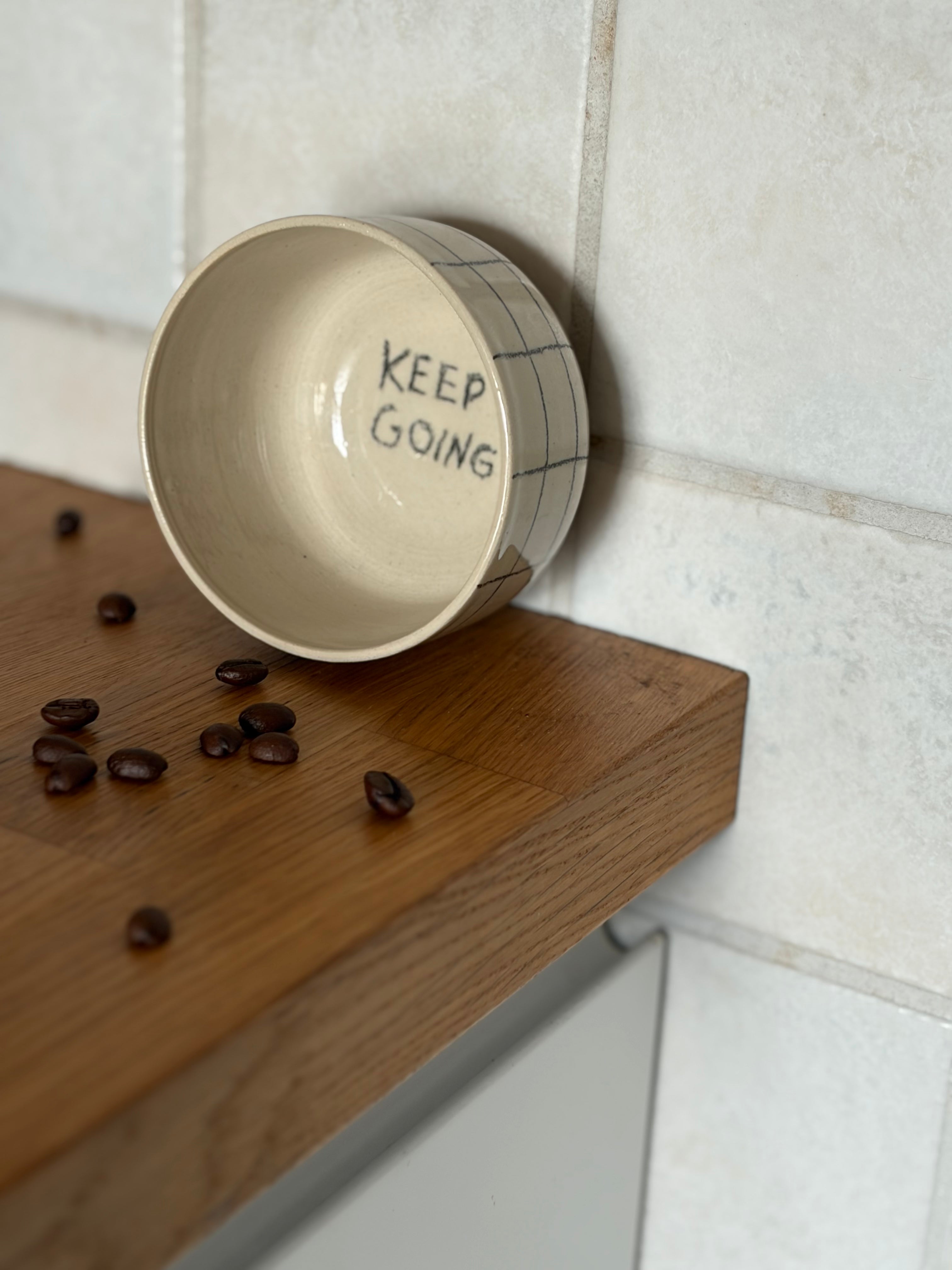 handgedrehter Keramikbecher an die wand gestellt damit man die Innschrift 'keep going' lesen kann. Von ausser schwarz kariert. 