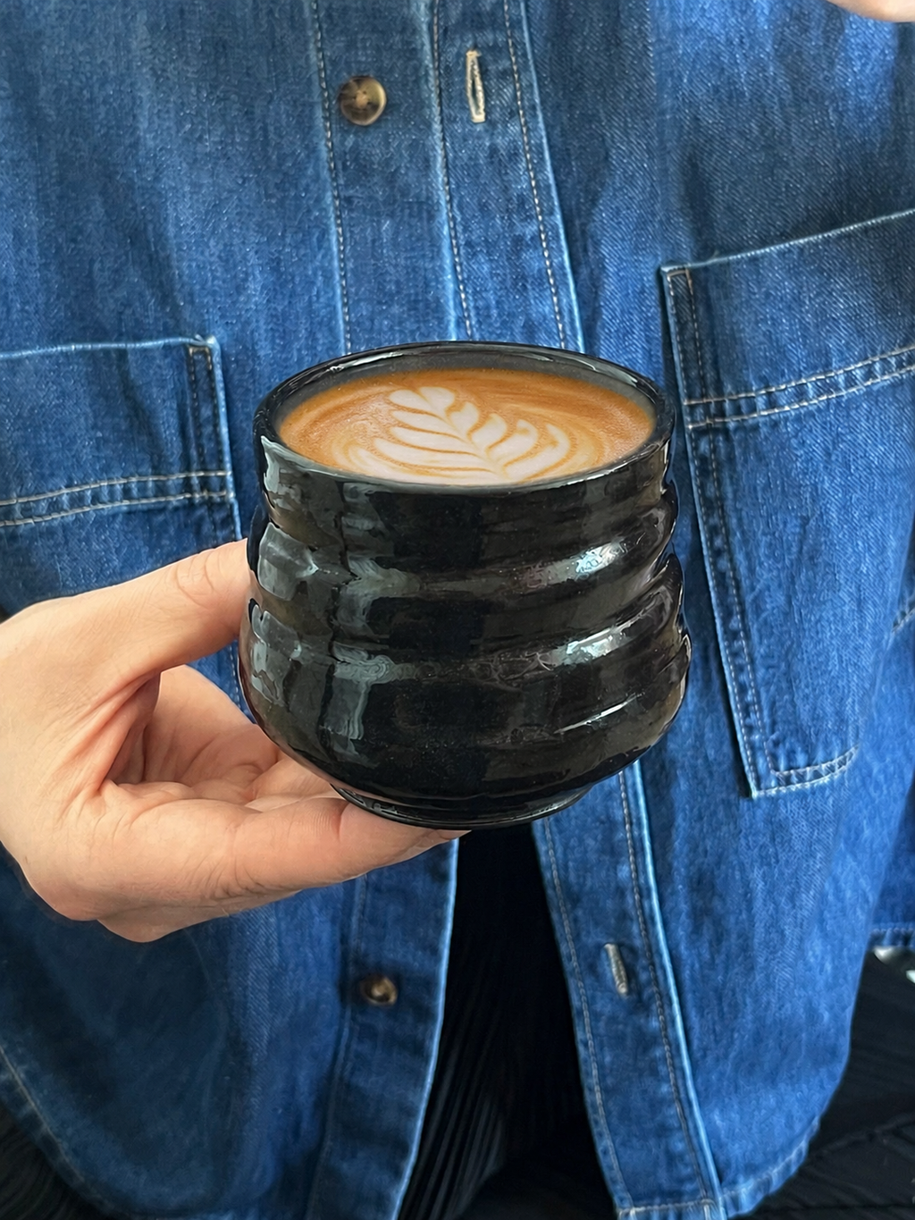 Handgedrehter Keramikbecher Black Void Cup von project.void._, in der Hand gehalten, mit Latte Art
