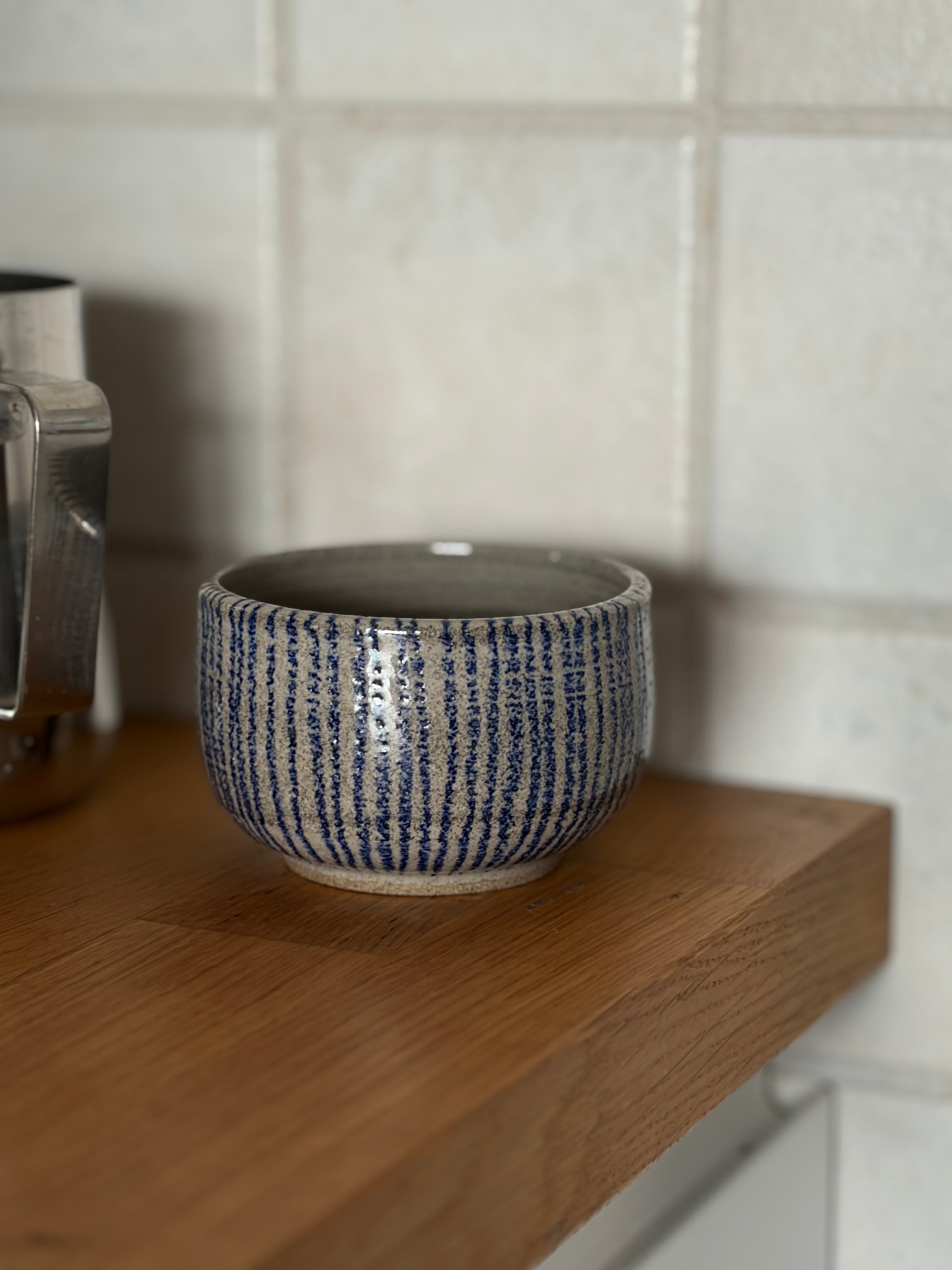 Nahaufnahme von handgemachtem Keramikbecher. Grauer Ton mit Blauen streifen