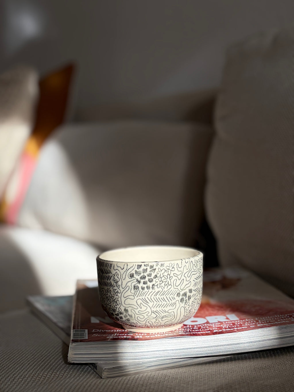 Handgedrehter Keramikbecher 'Daydream' mit handgemaltem Doodle-Muster in Schwarz, auf Sofa drapiert