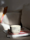 Handgedrehter Keramikbecher 'Daydream' mit handgemaltem Doodle-Muster in Schwarz, auf Sofa drapiert