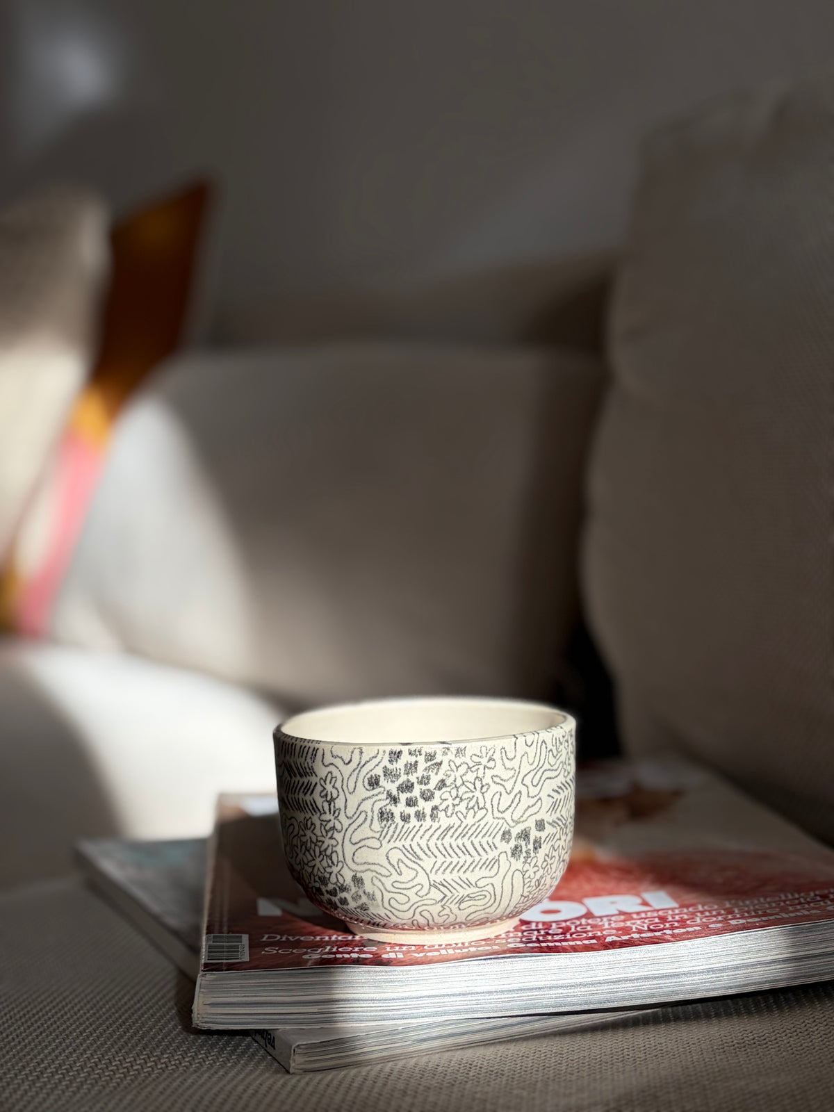 Handgedrehter Keramikbecher 'Daydream' mit handgemaltem Doodle-Muster in Schwarz, auf Sofa drapiert