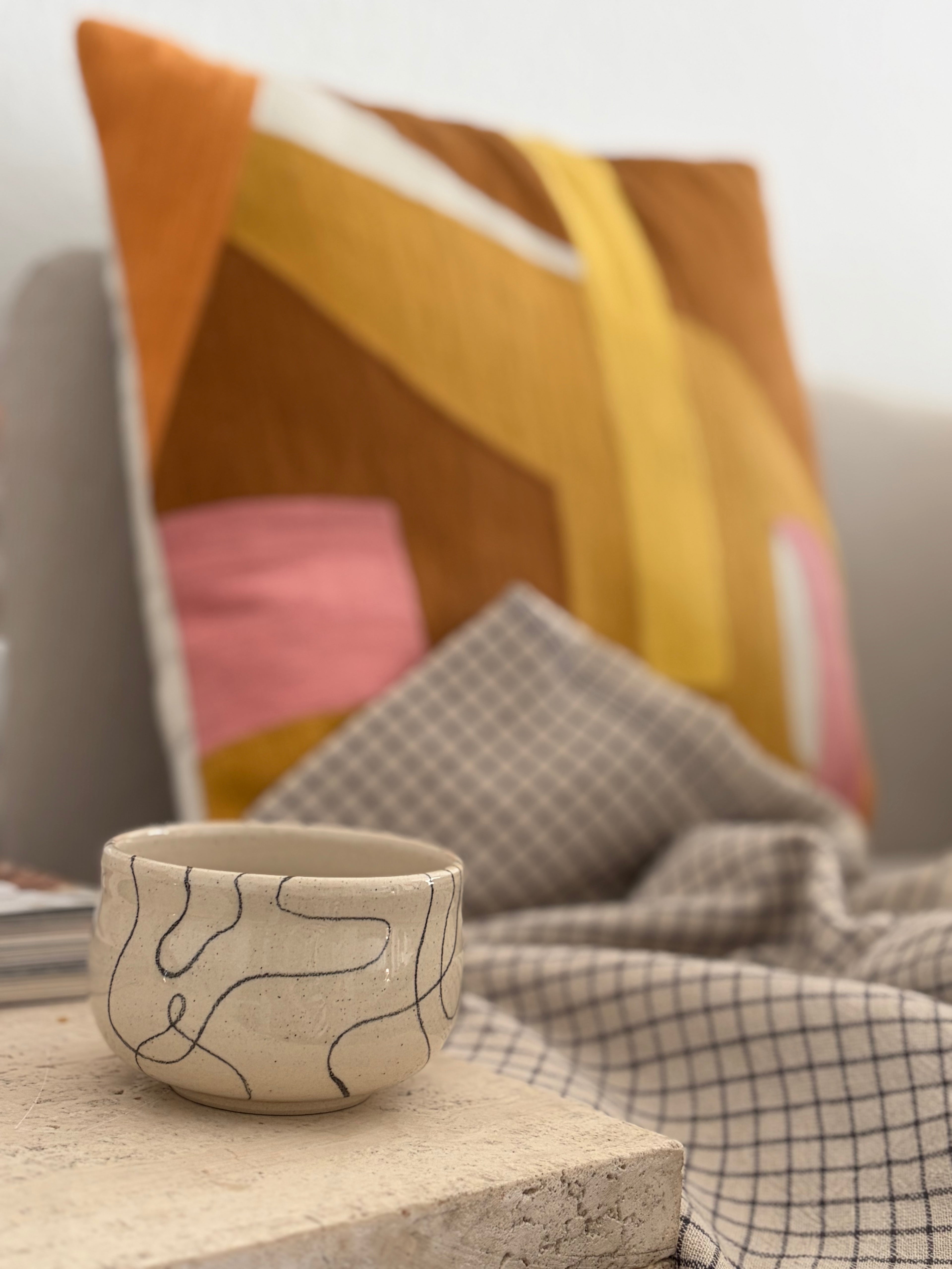 Handgedrehter Keramikbecher Flow Cup Wave mit geschwungenen Linien in schwarz, auf marmortisch vor bunten Kissen