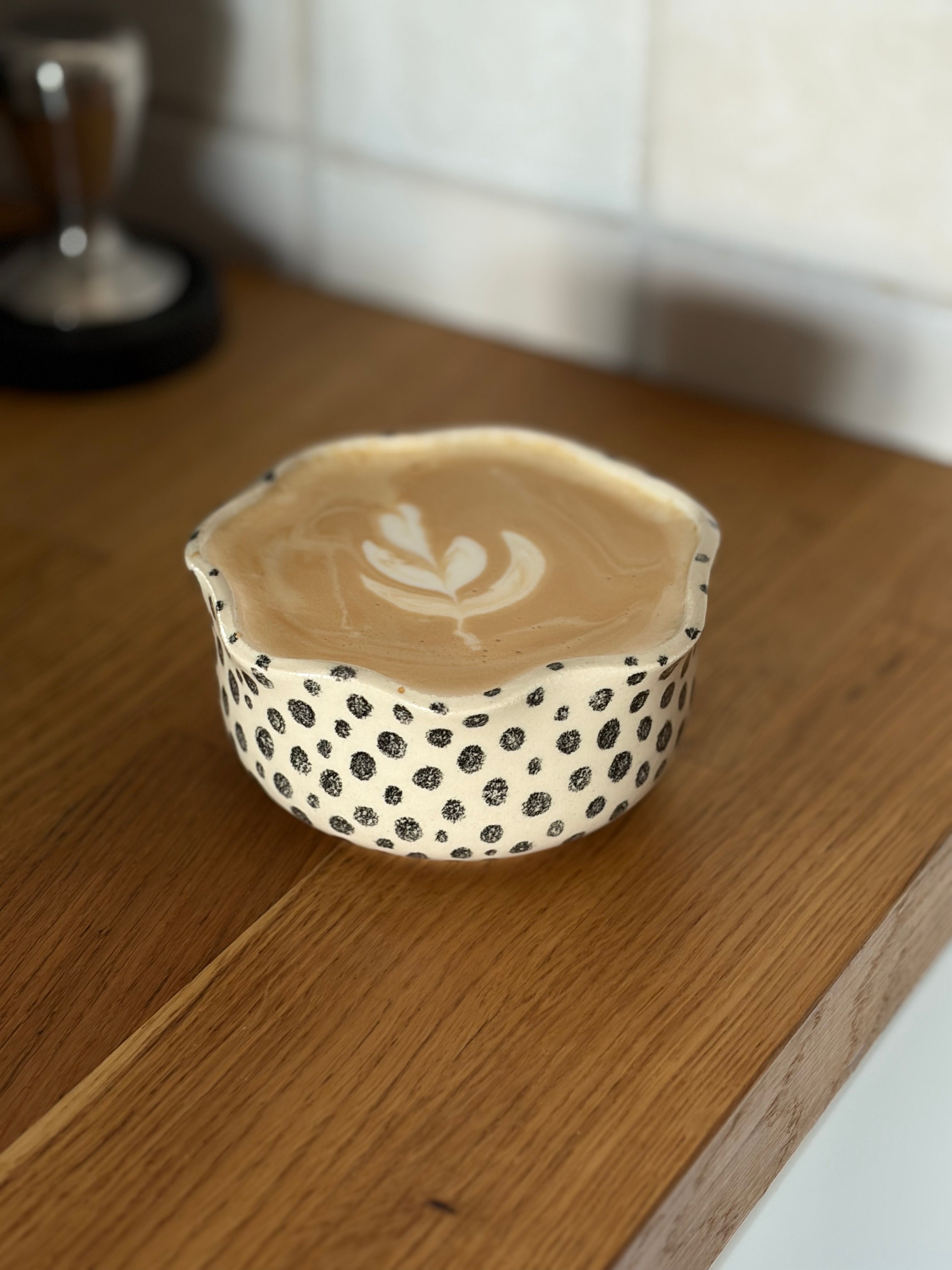 Ein handbemalter Keramikbecher, in Blumenform mit schwarzen Punkten gefüllt mit kaffee