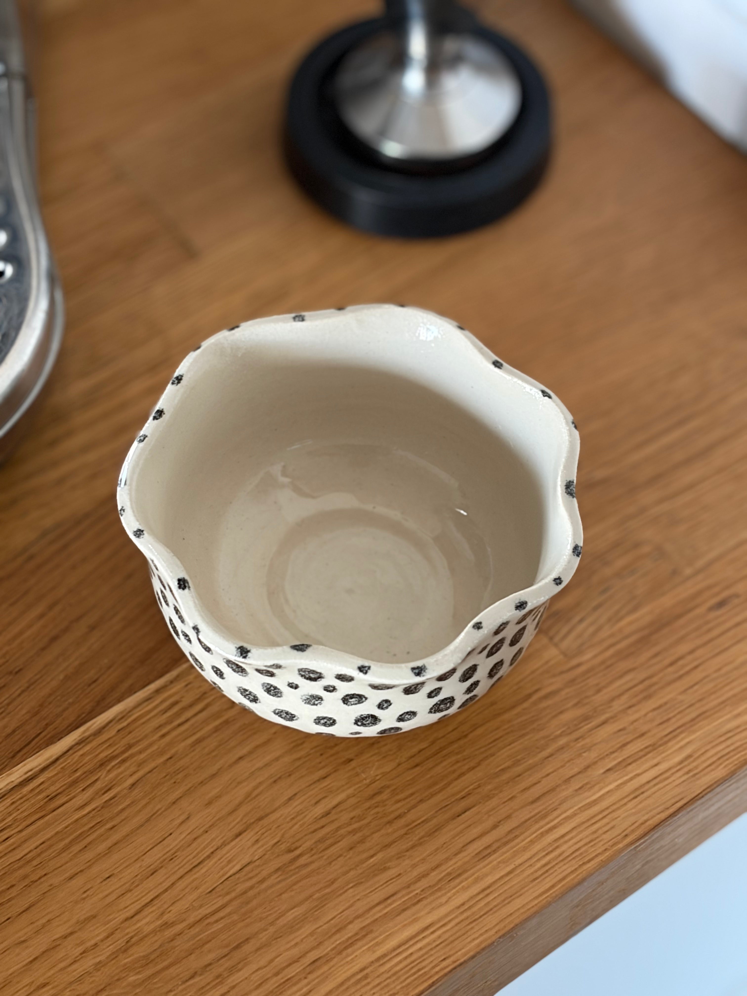 Die Innenansicht eines beigen Keramikbecher, man sieht seitlich handgemalte schwarze Punkte 