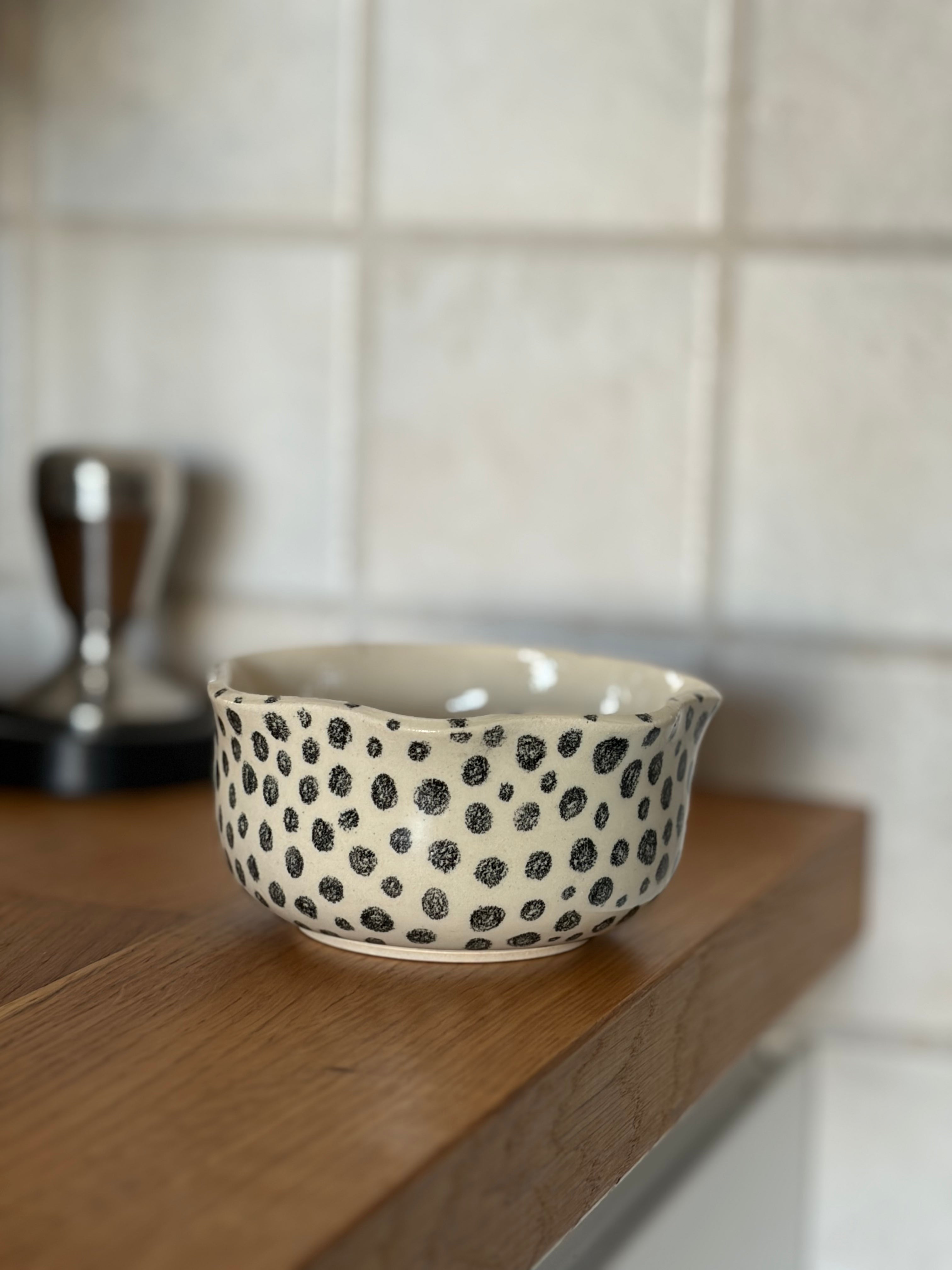 Handgemachter Keramikbecher in beige mit schwarzen Punkten bemalt in Kaffee-Ecke platziert 