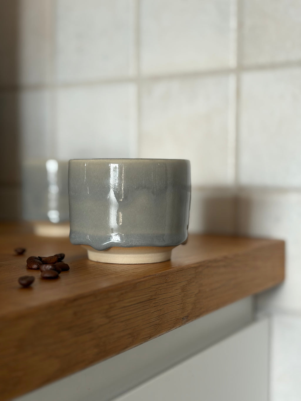 handgemachter Leramikbecher mit einer grauen drop Glasur auf Holzplatte 