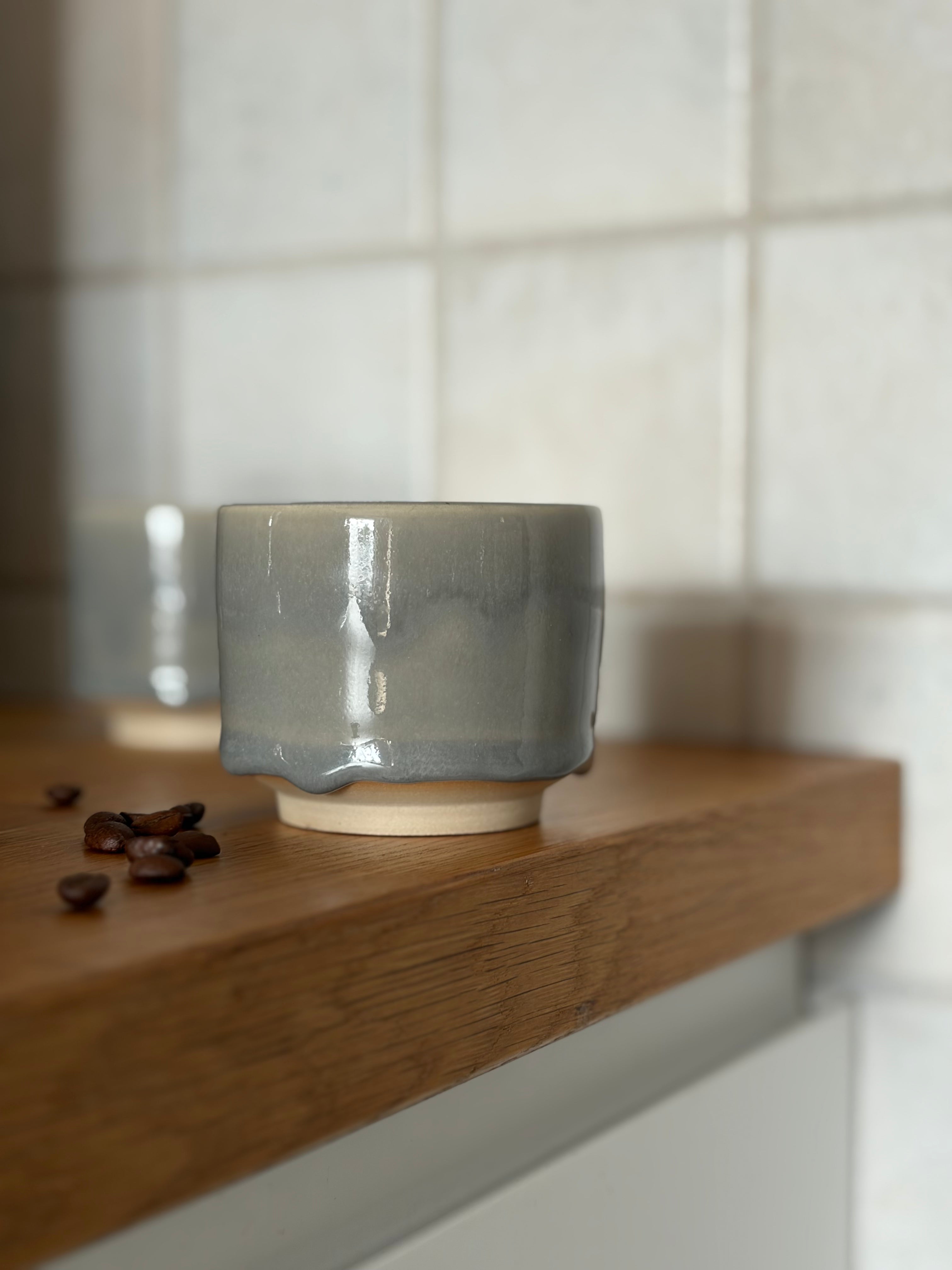 handgemachter Leramikbecher mit einer grauen drop Glasur auf Holzplatte 