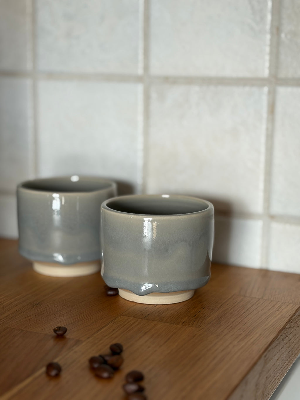 zwei Keramikbecher mit ruhiger grauer Glasur auf weißem ton. mit Kaffeebohnen auf holzplatte 