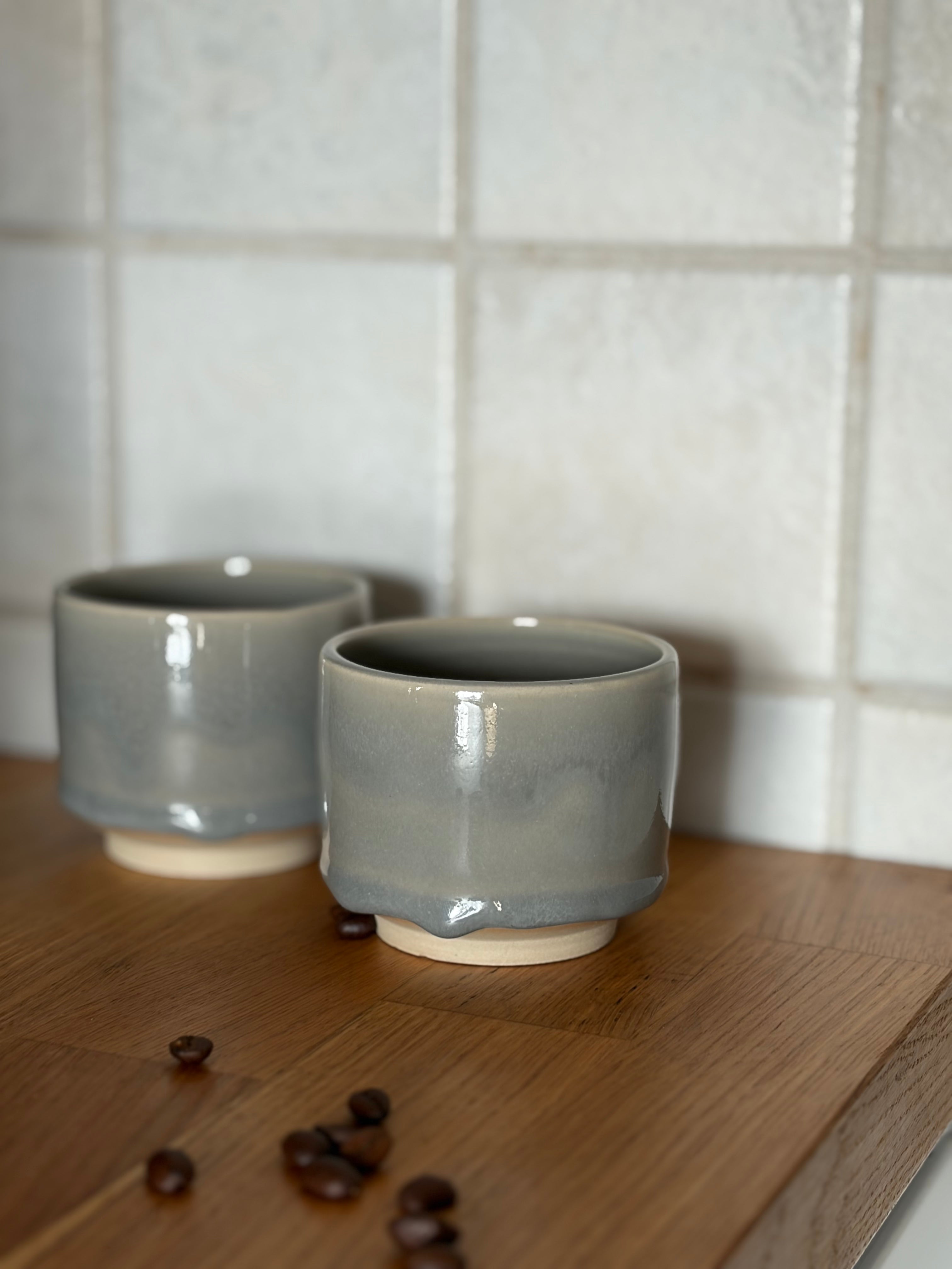 zwei Keramikbecher mit ruhiger grauer Glasur auf weißem ton. mit Kaffeebohnen auf holzplatte 