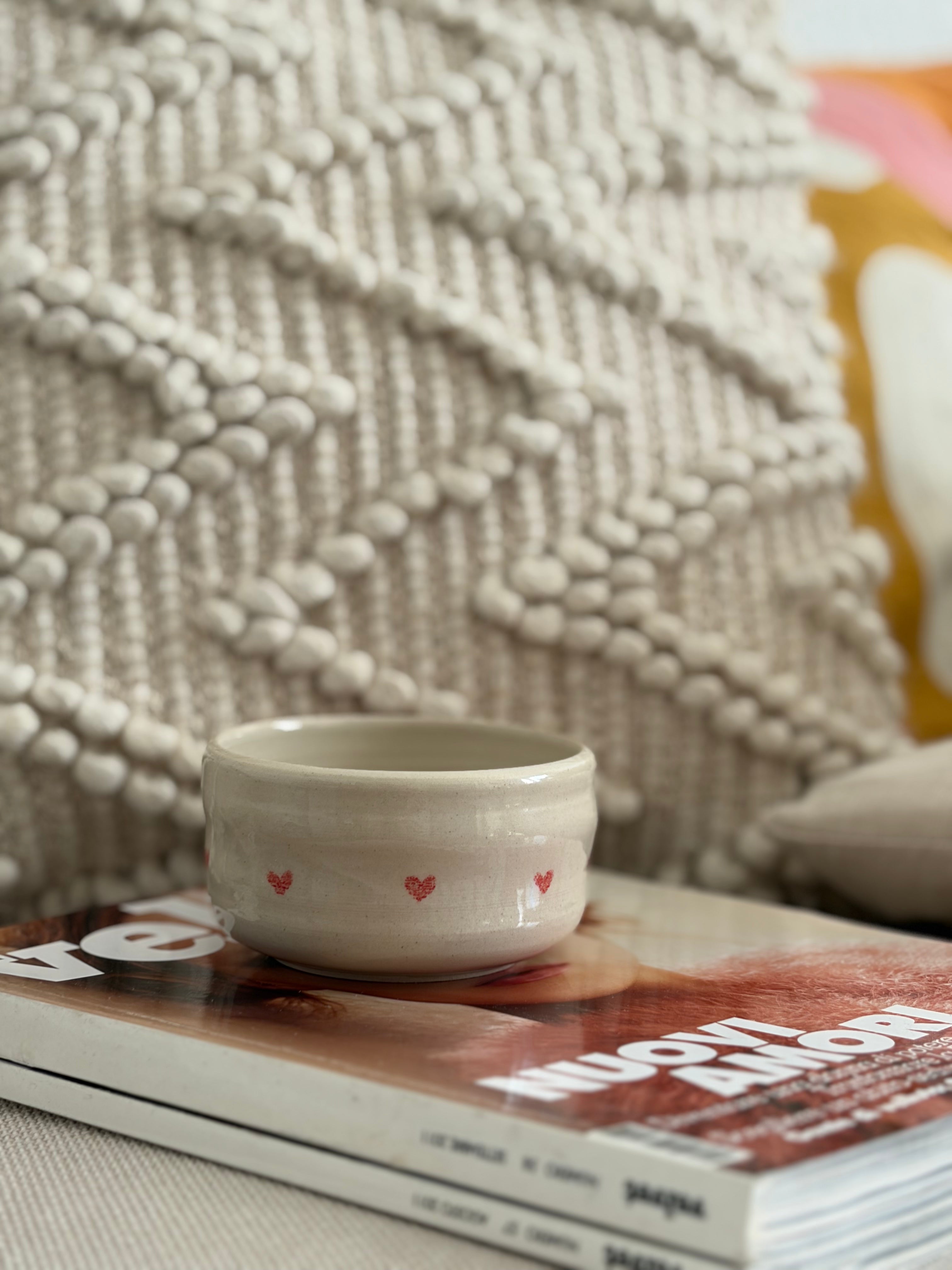 Handgedrehter Keramikbecher Tiny Hearts Cup mit kleinen roten Herzchen, auf Magazin vor gewebtem Textil-Hintergrund